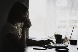 A woman holding a cup, sitting at a desk and working on her laptop, trying to find information about an estate moving company.