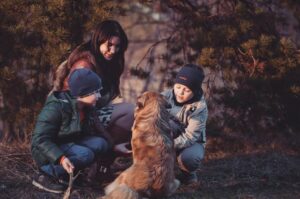 A woman with two boys in nature playing with a dog during fall