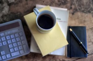 Cup of coffee, calculator, notebook, pen, laptop.