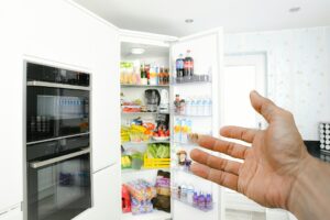 Hand pointing to open fridge, filled with food and beverages.