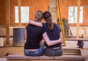 Who knows how much money you will have to spend on remodeling? Two girls hugging after committing one of the mistakes first-time home buyers make.