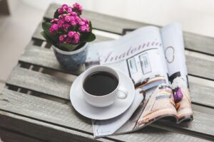 A magazine next to a cup of coffee and a flower pot.