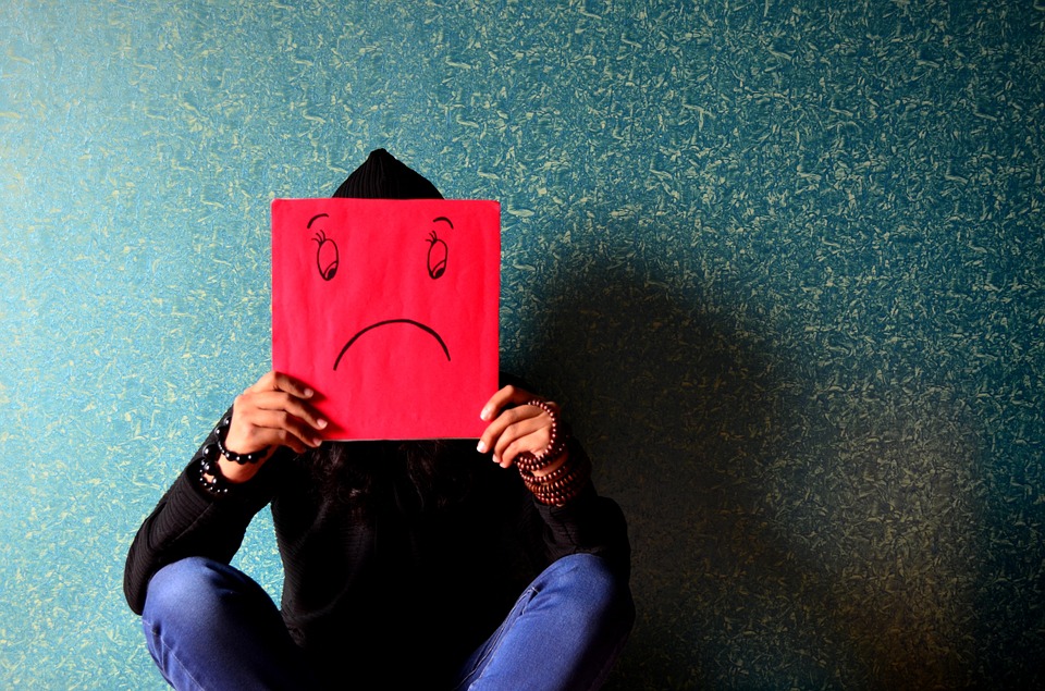 A man holding a red paper with a sad emoticon on it.