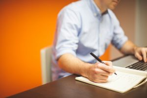 man looking at computer and writing